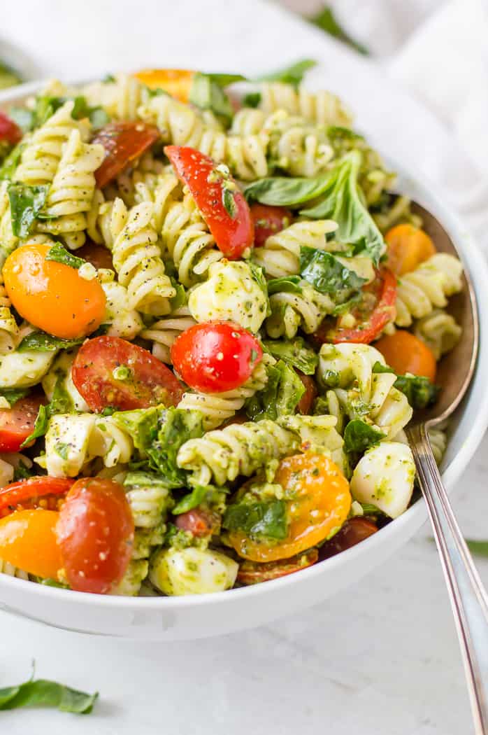 Pesto veggie pasta salad in a white bowl with a spoon. 