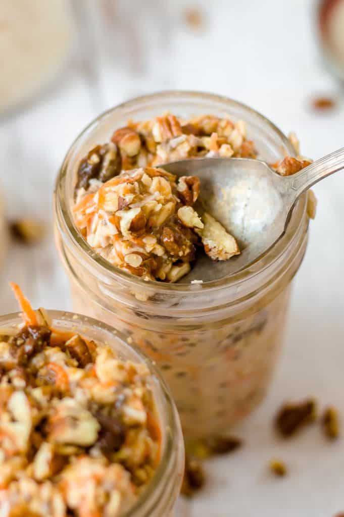 Carrot cake overnight oats in jelly jars. A spoon is taking a scoop of oats out of one of the jars.