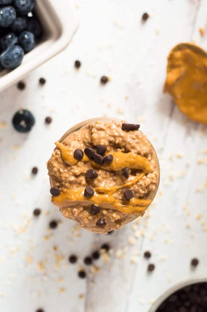 A serving of sweet potato chocolate peanut butter oats in a jar topped with more peanut butter and chocolate chips. 