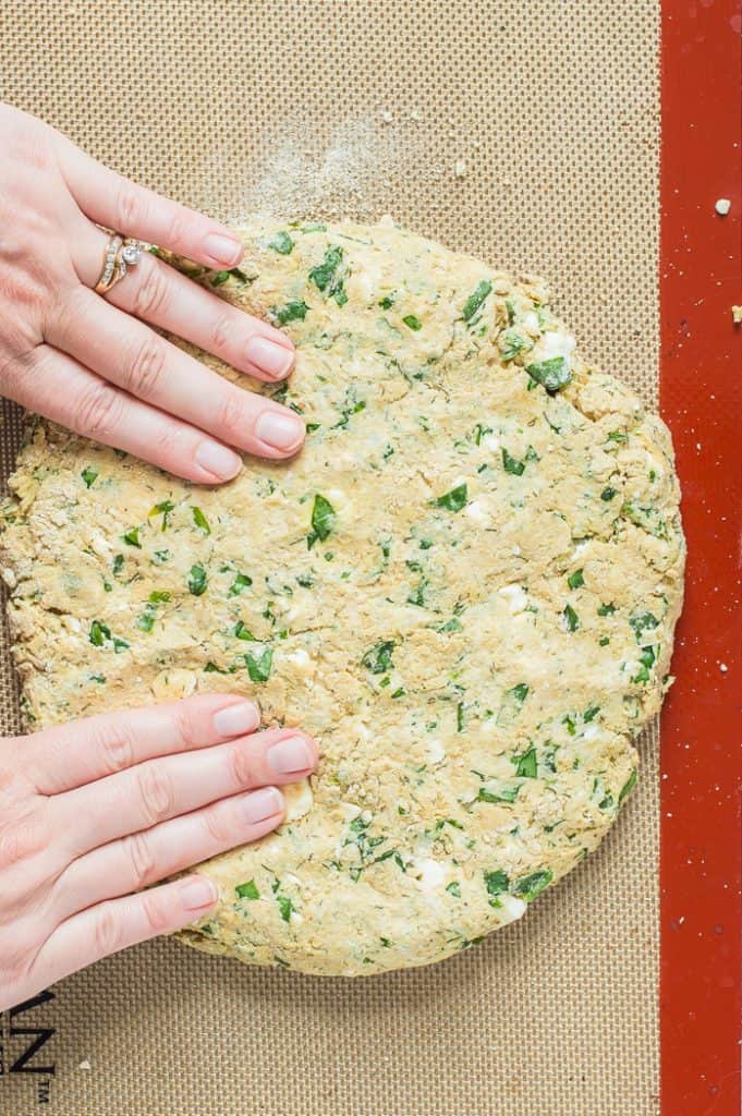 Two hands forming the dough for feta spinach scones into a circle on a baking sheet.