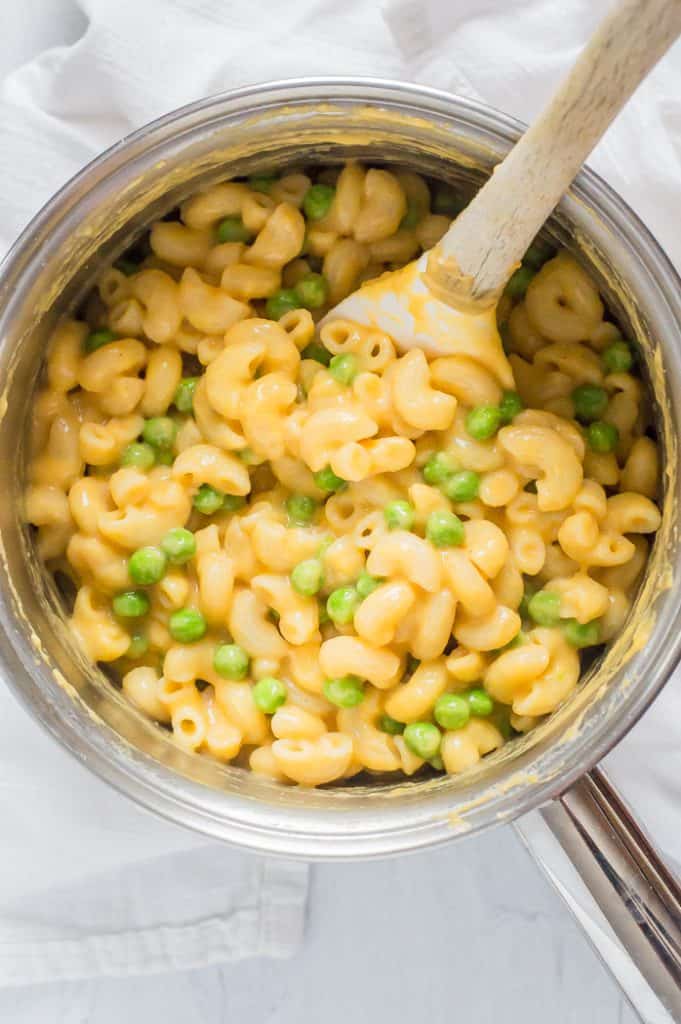 Veggie-loaded mac and cheese in a sauce pot with a spatula. 