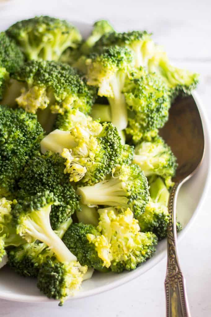 A bowl of steamed broccoli with a metal spoon.