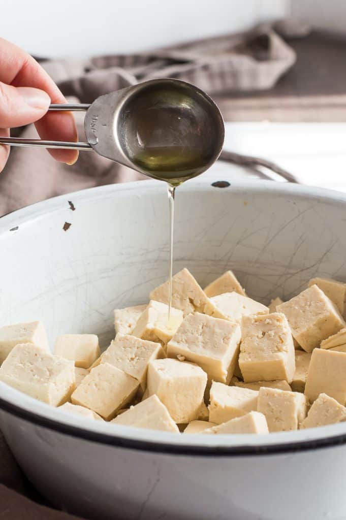 Tofu being drizzled with oil in a bowl.