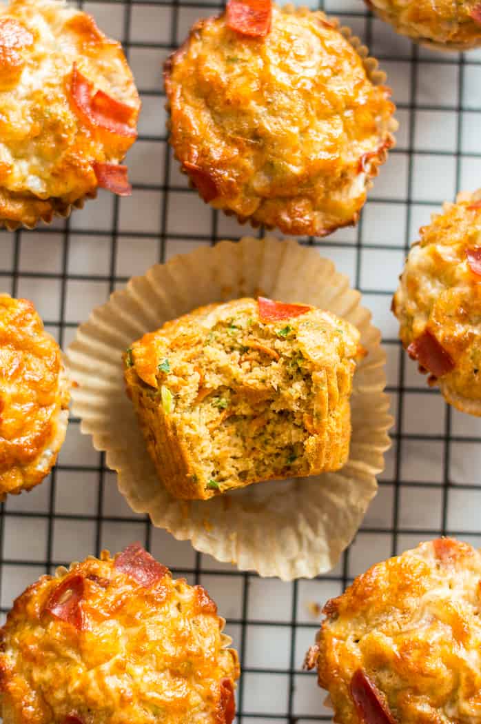 Veggie-loaded pizza muffins on a cooling rack. One muffin has a bite taken out of it.