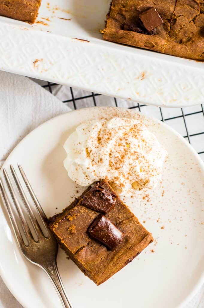 A pumpkin brownie on a plate with a fork and whipped cream.