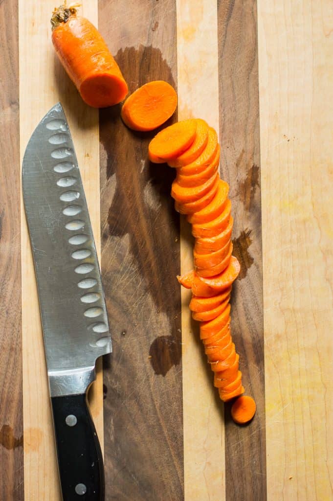 A carrot on  a cutting board cut into slices. There is a knife on the cutting board next to the carrot. 