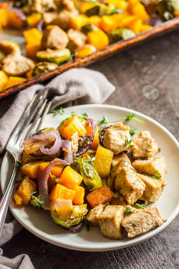 Chicken and butternut squash dinner on a plate with a fork and the rest of the sheet pan meal is in the background.