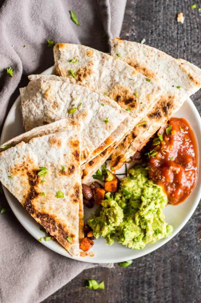 Black bean sweet potato quesadilla cut into pieces on a plate with salsa and mashed avocado.