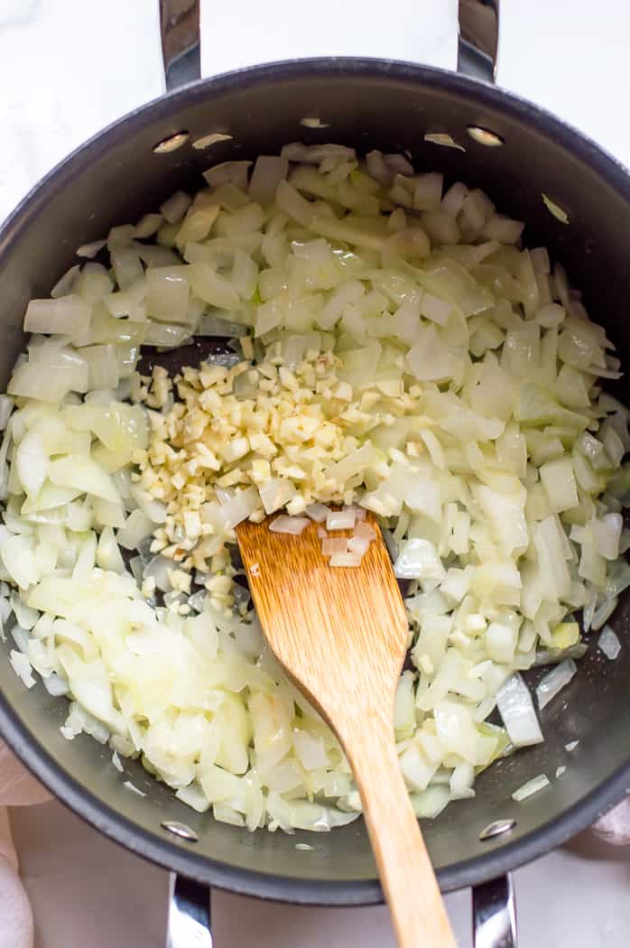 Chopped onions and garlic in a pot with a wooden spoon.