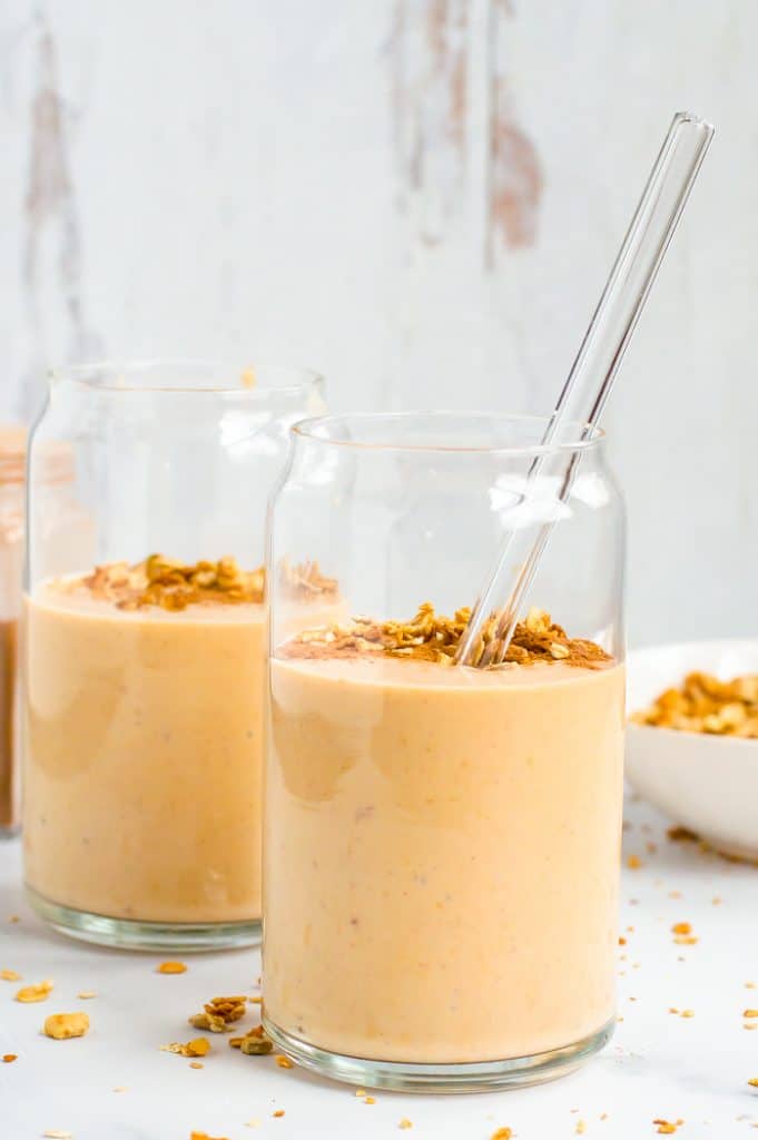 Sweet potato smoothie in two glasses. They are topped with granola and one has a straw in it.
