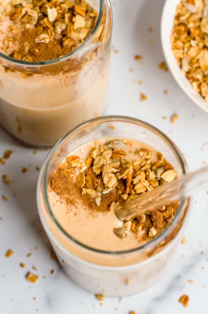 Sweet potato smoothie in two glasses and topped with granola. One glass has a straw in it.