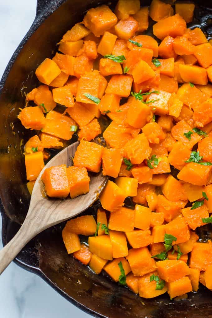 Sautéed butternut squash in a cast iron skillet with a wooden spoon. 