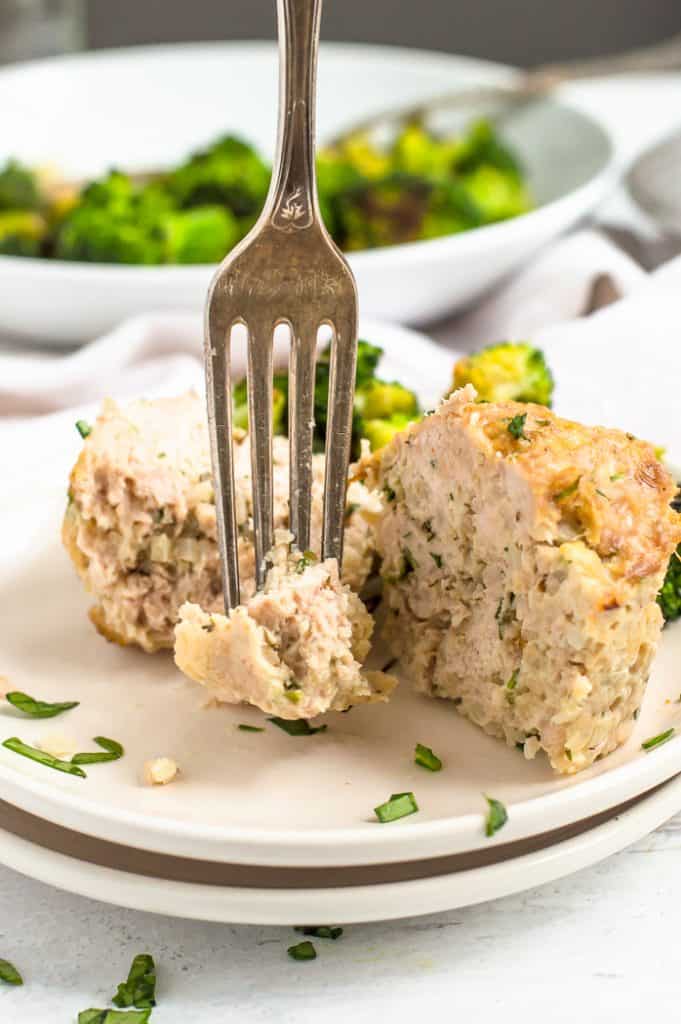 A turkey mini meatloaf on a plate with broccoli. A fork is taking a bite of meatloaf.