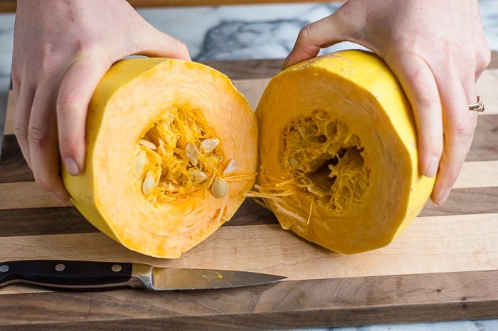 Two hands cracking open a raw spaghetti squash on a cutting board.