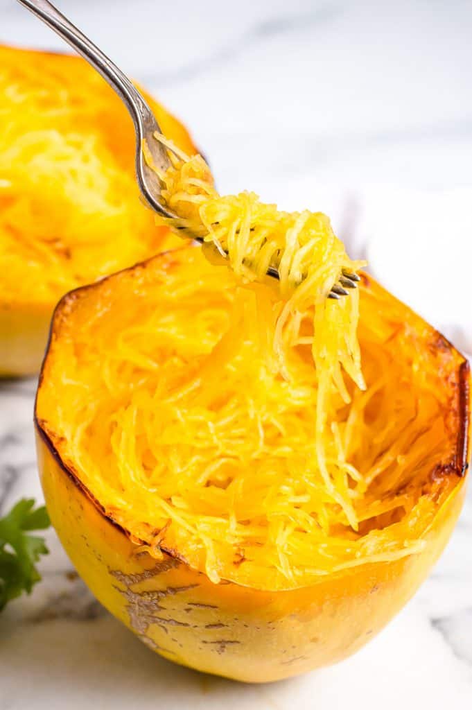 A cooked spaghetti squash with a fork twirling some cooked stands on it. 