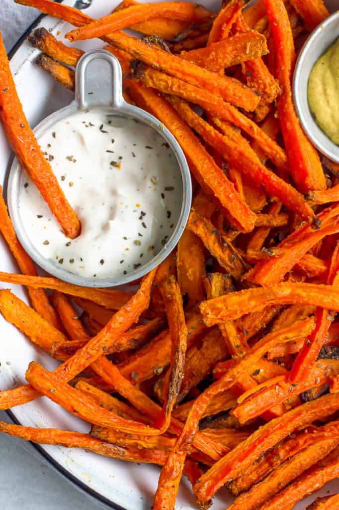 A plate of carrot fries with a small dish of ranch dressing with a carrot fry in it.
