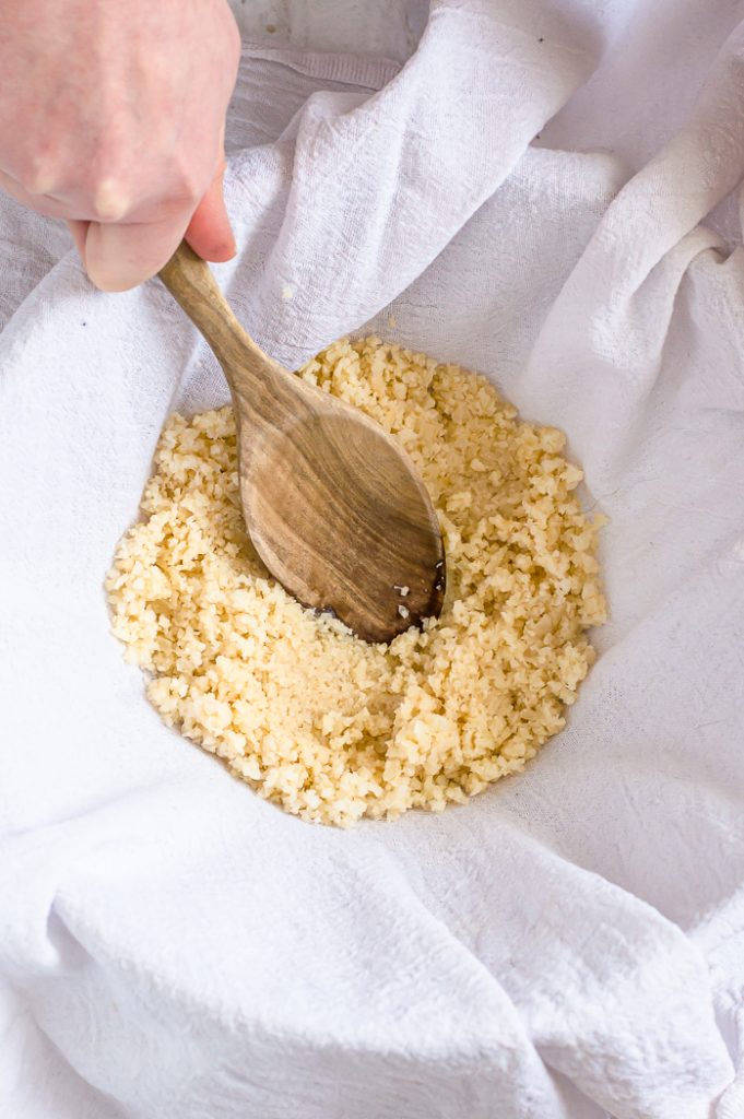 Riced Cauliflower in a tea towel with a spoon or hand pushing liquid out