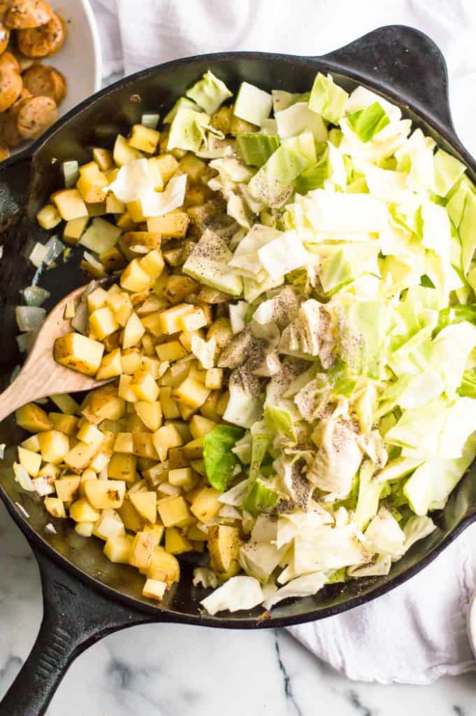 Potatoes and cabbage in a skillet with salt and pepper sprinkled over the top.