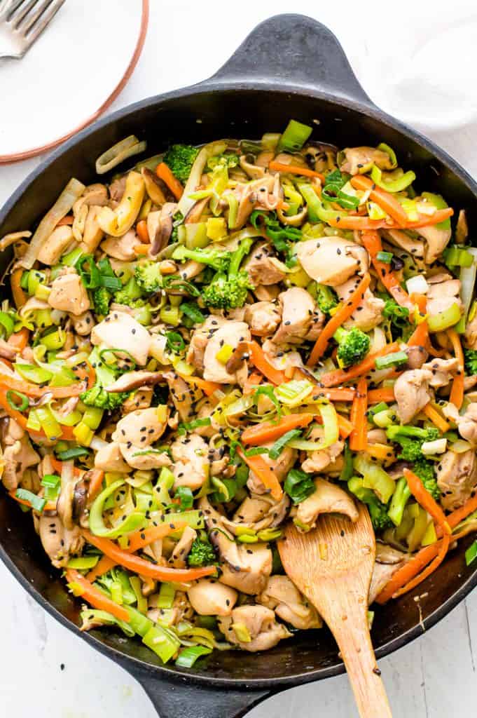 Chicken and Leek stir fry in a cast iron skillet with a wooden spoon.