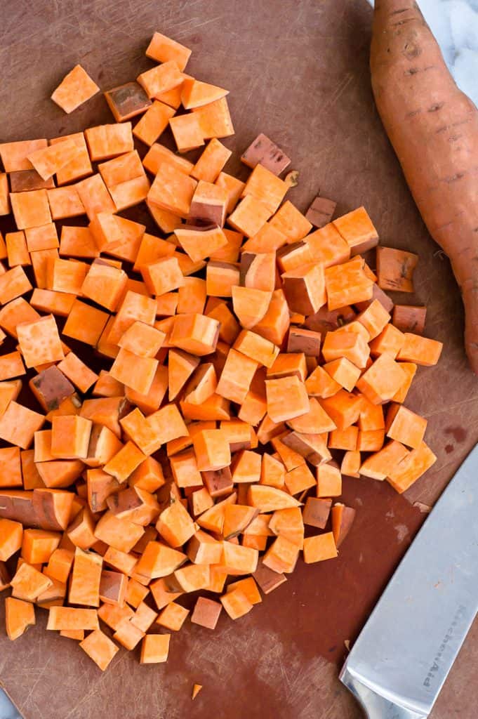 Diced sweet potato on a cutting board with a knife.