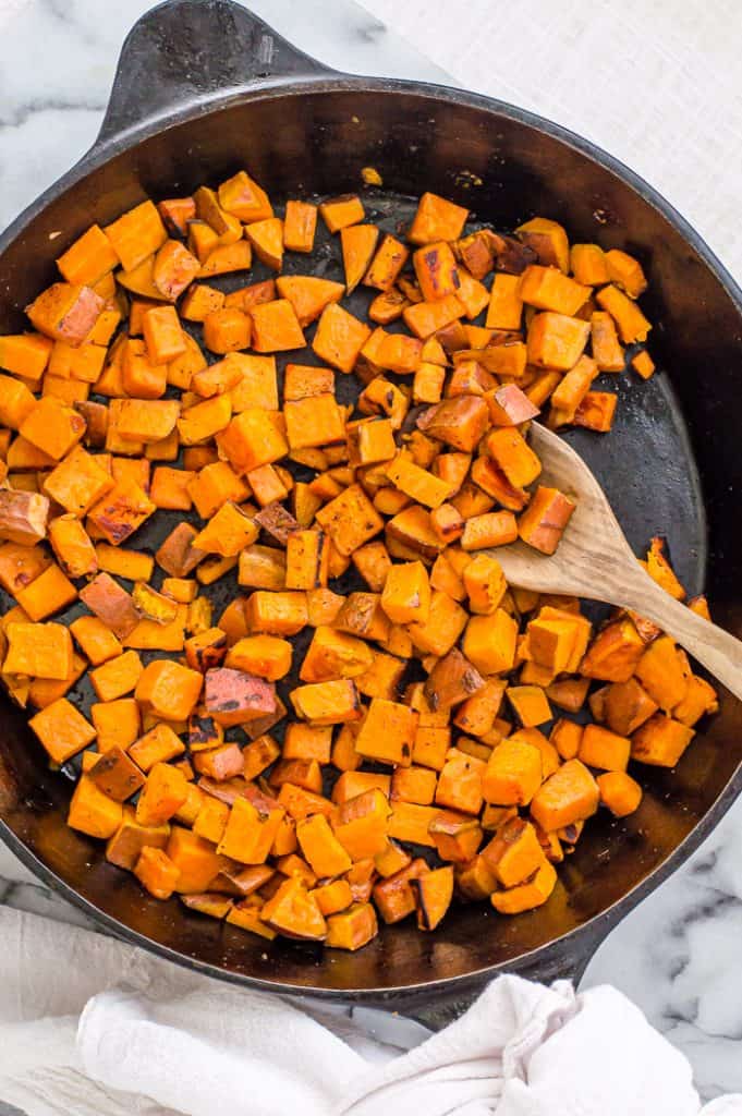 Sweet potatoes in a cast iron skillet with a wooden spoon.