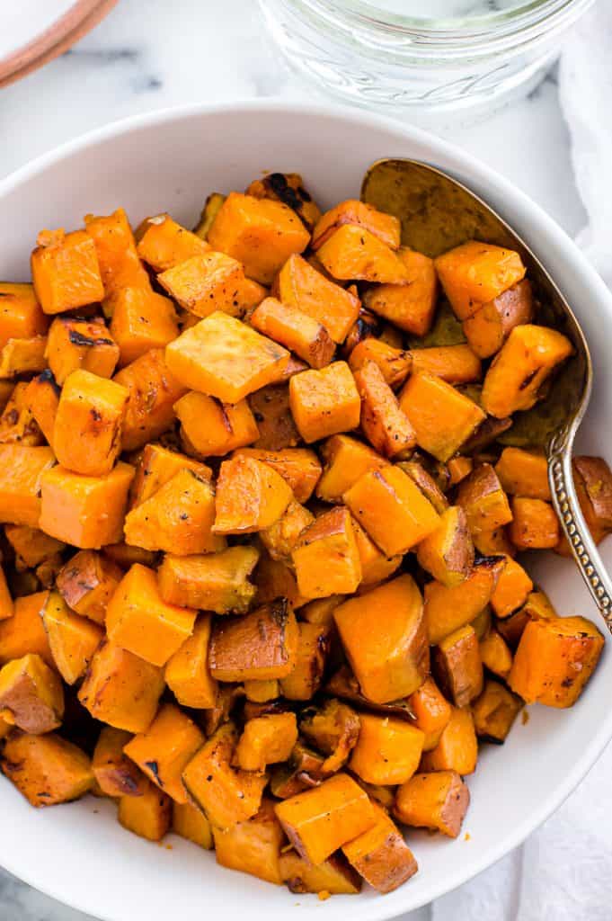 Skillet sweet potatoes in a white bowl with a metal serving spoon.