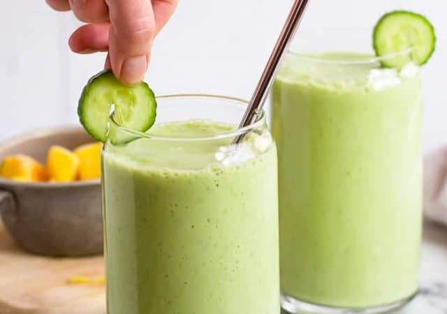 Putting a slice of cucumber on a glass with Mango Pineapple Cucumber Smoothie