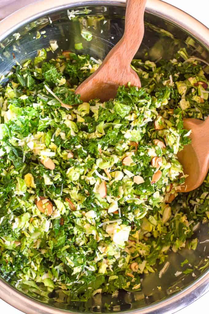 Lemony kale + shaved Brussel sprout salad in a big bowl with large wooden salad forks.