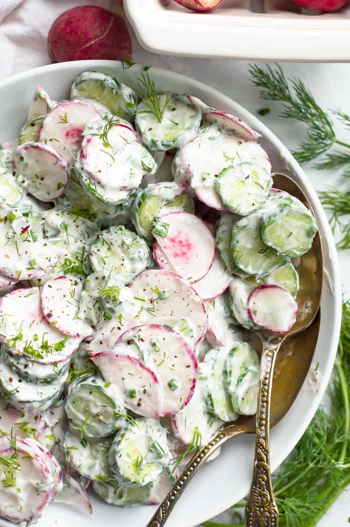 Creamy Cucumber radish salad in a bowl with two spoons.

It is on a white table with fresh radishes and fresh dill next to it.