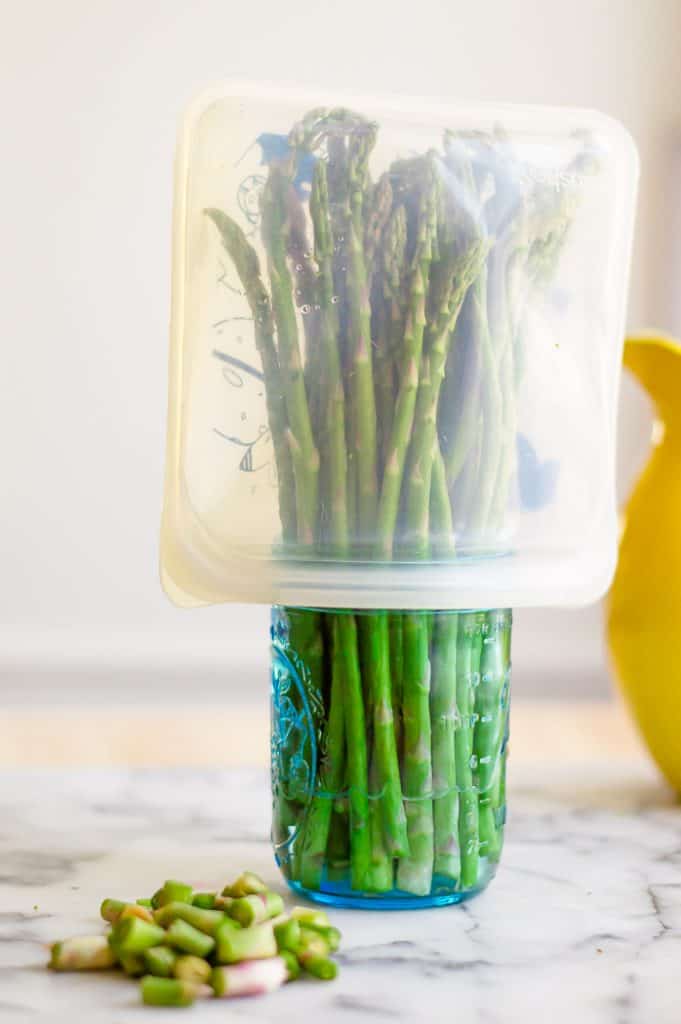 Fresh asparagus in a mason jar with a silicone bag over the top.