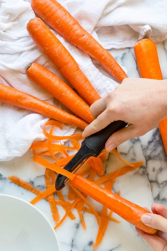 A hand peeling a bunch of carrots.