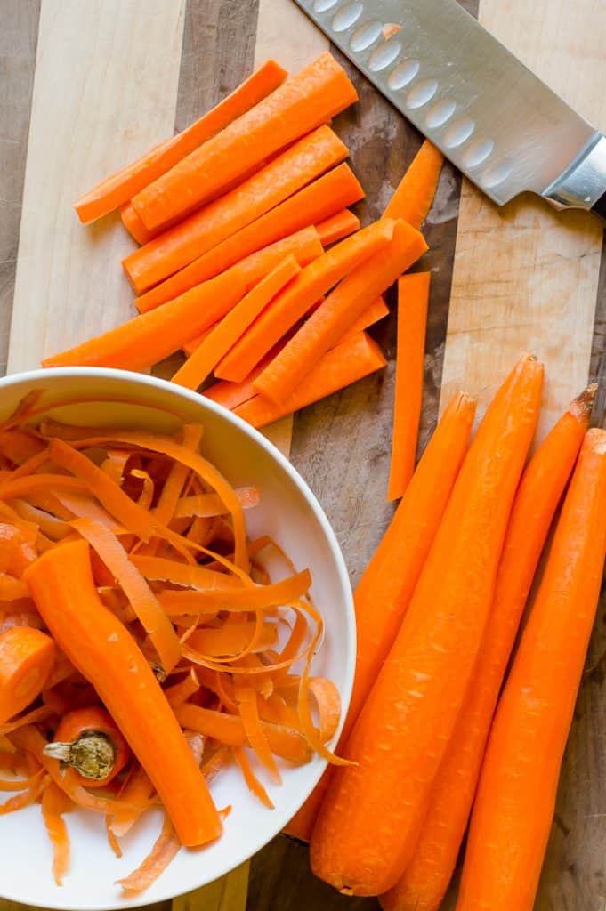 Peeled carrots on a cutting board. One carrot has been cut into sticks.