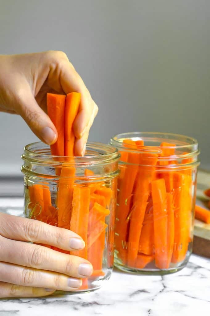 A hand placing cut carrots into 2 mason jars