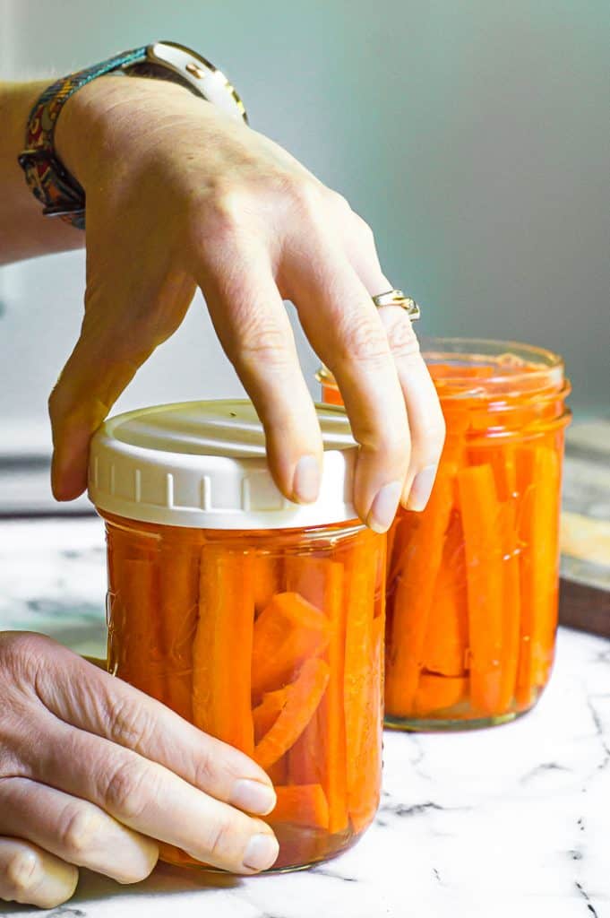 A hand putting a lid on a jar of cut carrots.