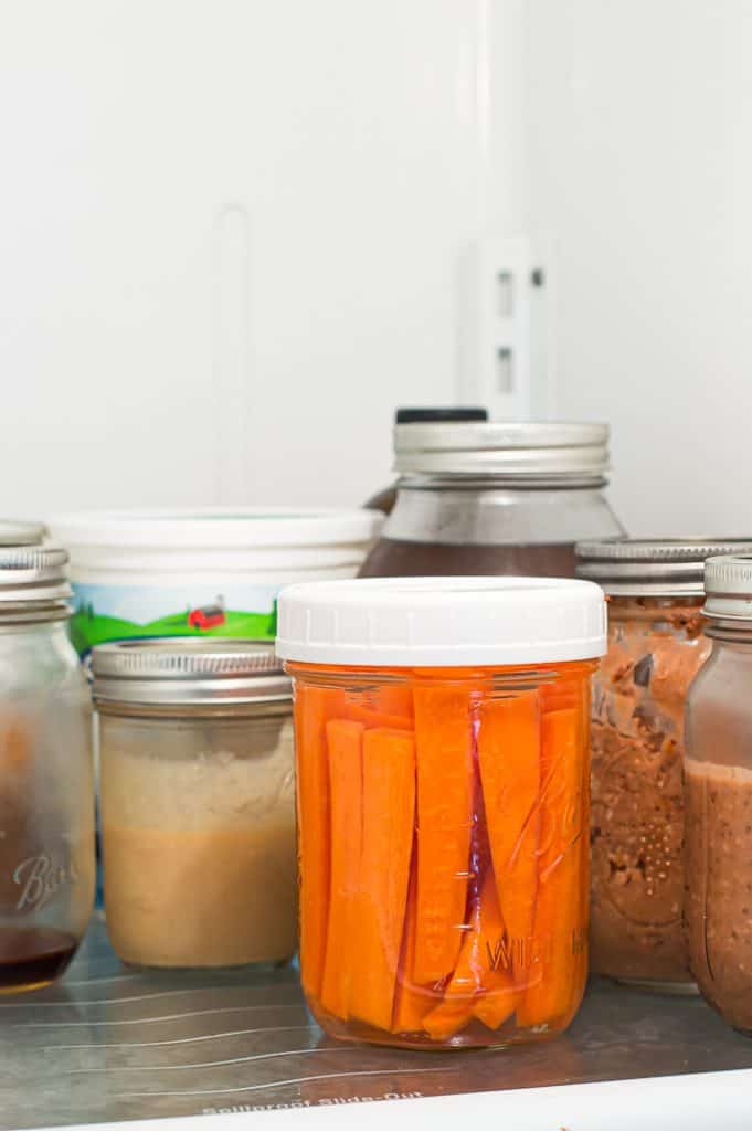 A jar of cut carrots in a fridge with other jars of food.