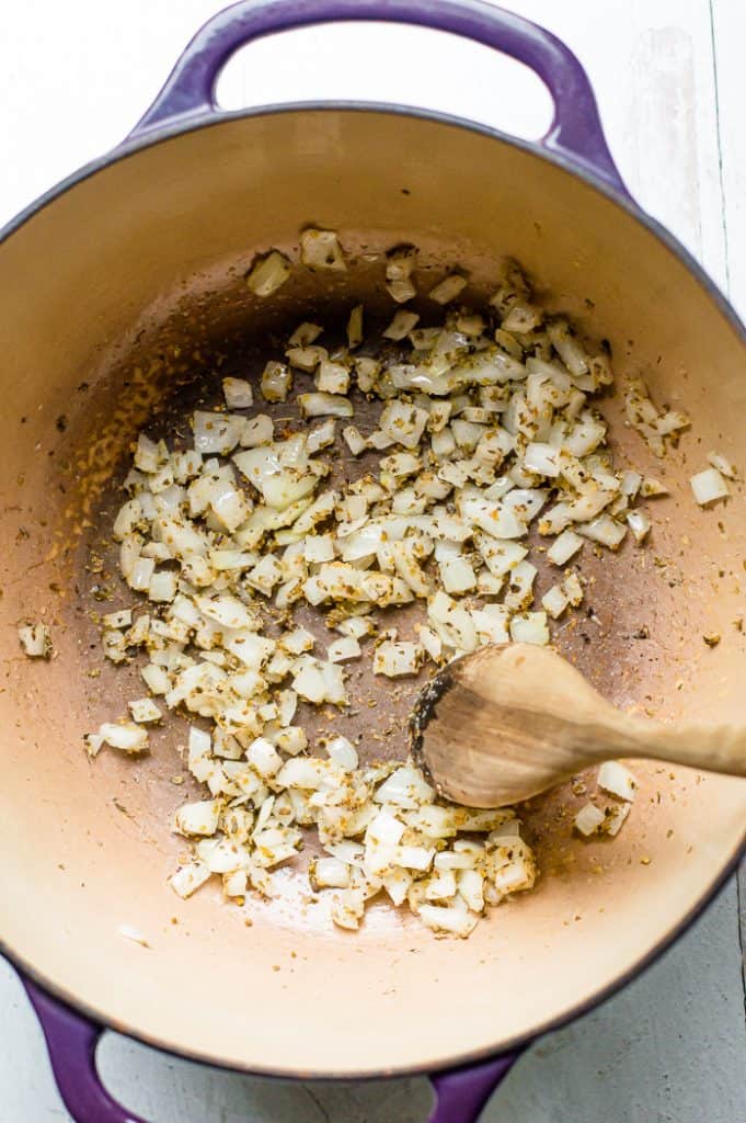 Diced onions with seasoning in a saucepan with a wooden spoon.