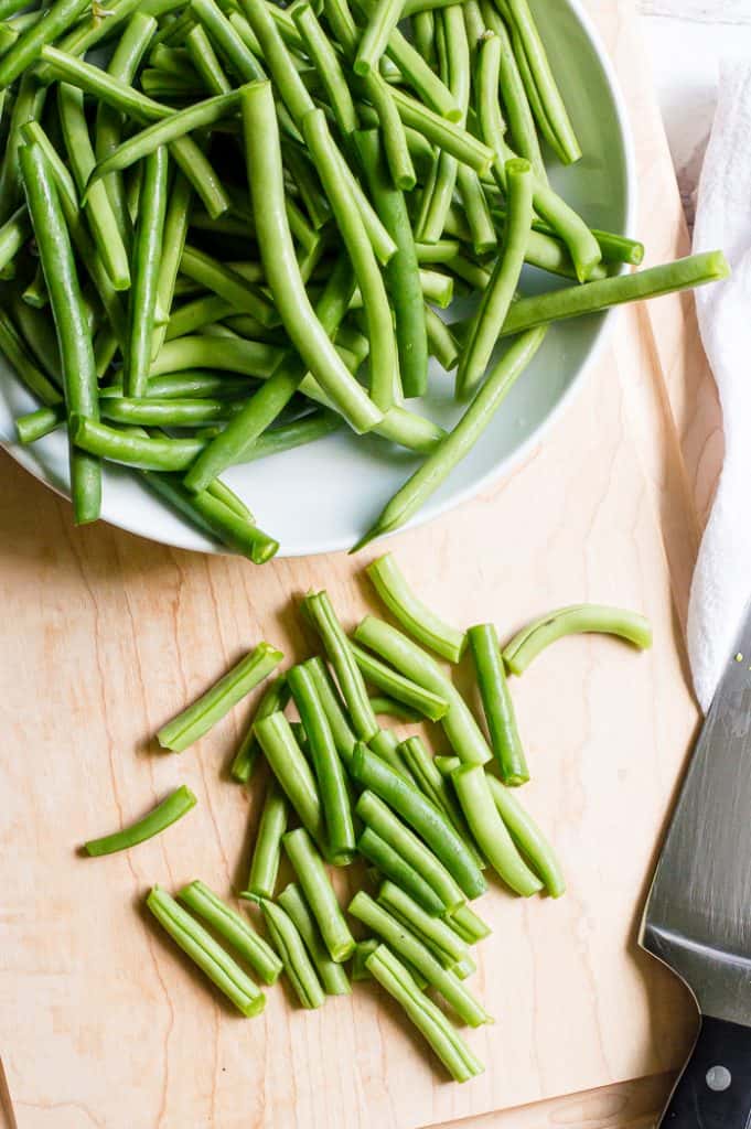 Fresh green beans on a cutting board with a knife, cut into bite-sized pieces.