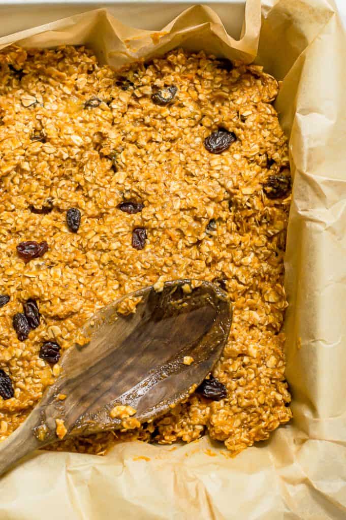 Sweet potato banana oatmeal bar mixture being spread into a prepared baking pan with a wooden spoon.