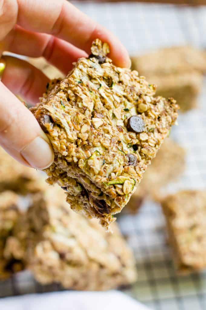 A hand holding a banana zucchini oatmeal bar.  The rest of the bars are blurred in the background.