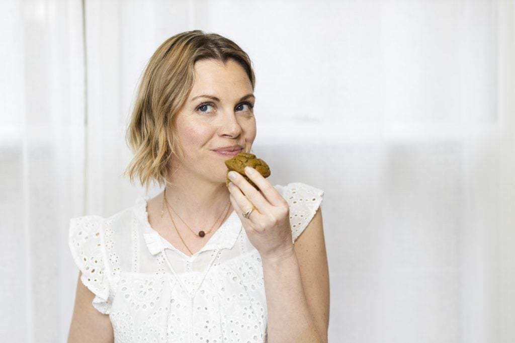 Woman in a white shirt eating a muffin.