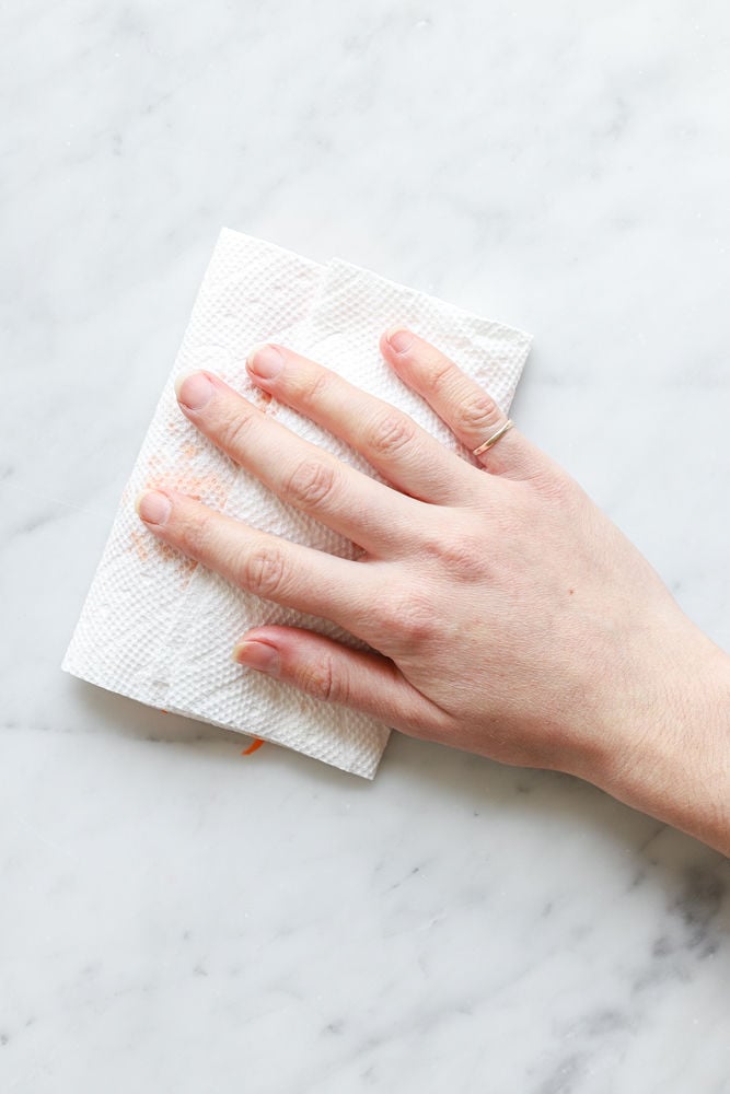 A hand pressing down on grated carrot wrapped in paper towel