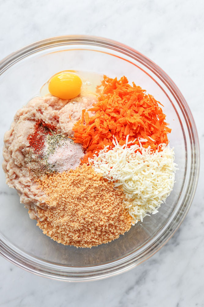 Ingredients for chicken carrot meatballs in a glass bowl before being mixed.