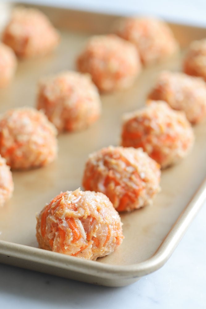 Chicken carrot meatballs on a lined baking sheet before baking.