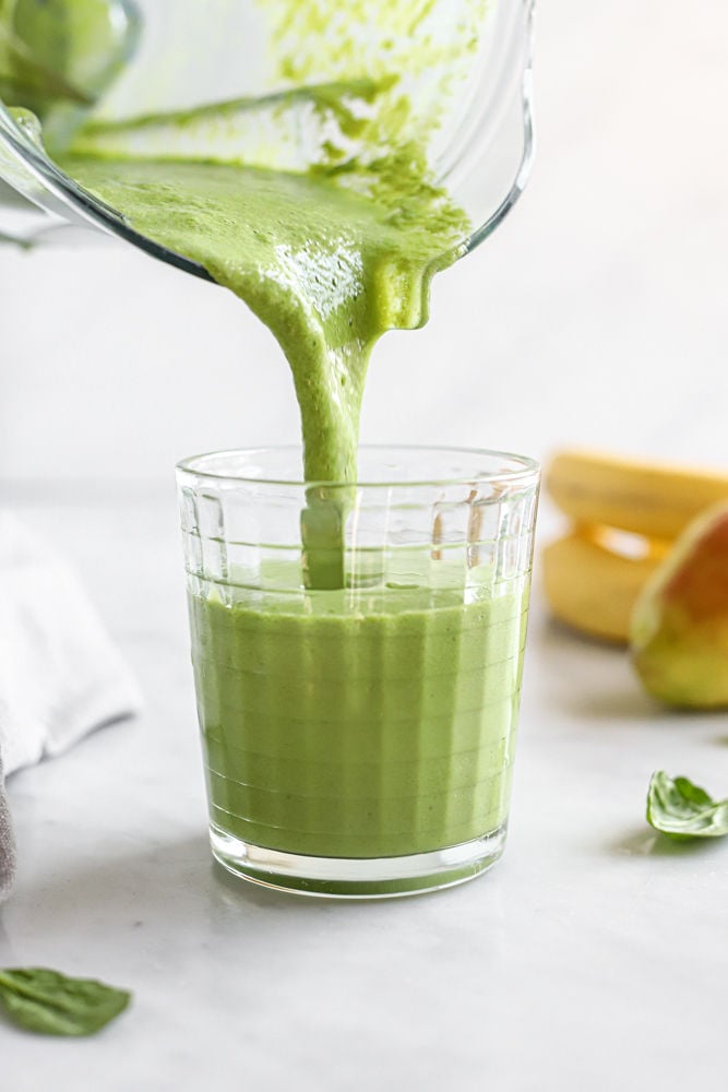 Spinach pear smoothie being poured into a glass from a blender.