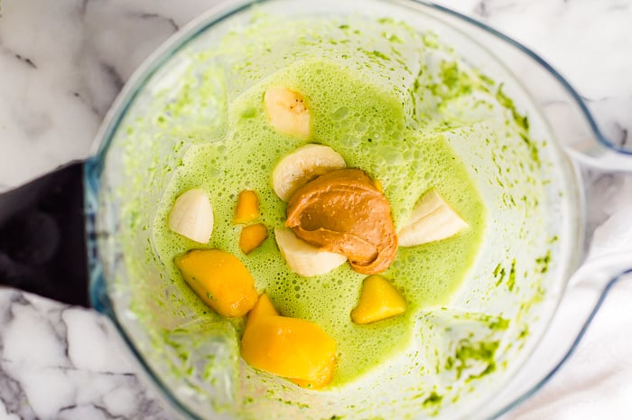 Blended spinach, kale, yogurt and milk in a blender with mango, sliced banana and peanut butter on top.