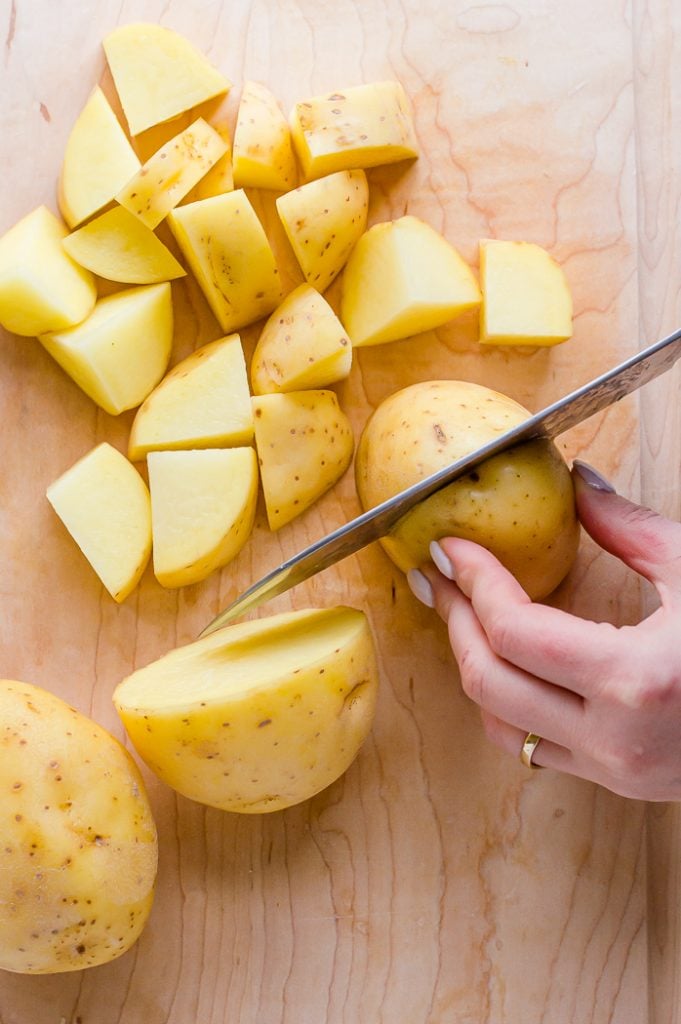 Yukon gold potatoes on a cutting board. A person is cutting a potato into pieces.