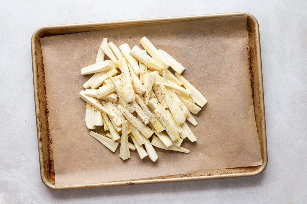 Peels and cut parsnips piled on a lined baking sheet.