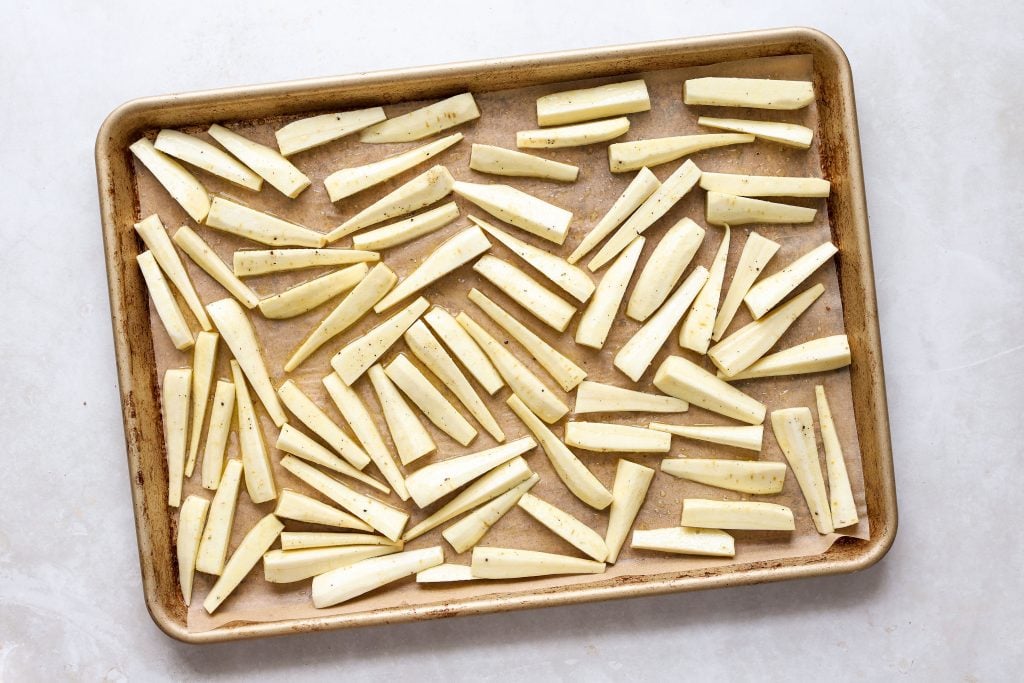 Peeled and cut parsnips spread out in a baking sheet.