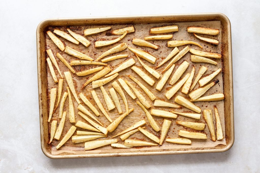 Roasted parsnip fries on a lined baking sheet.