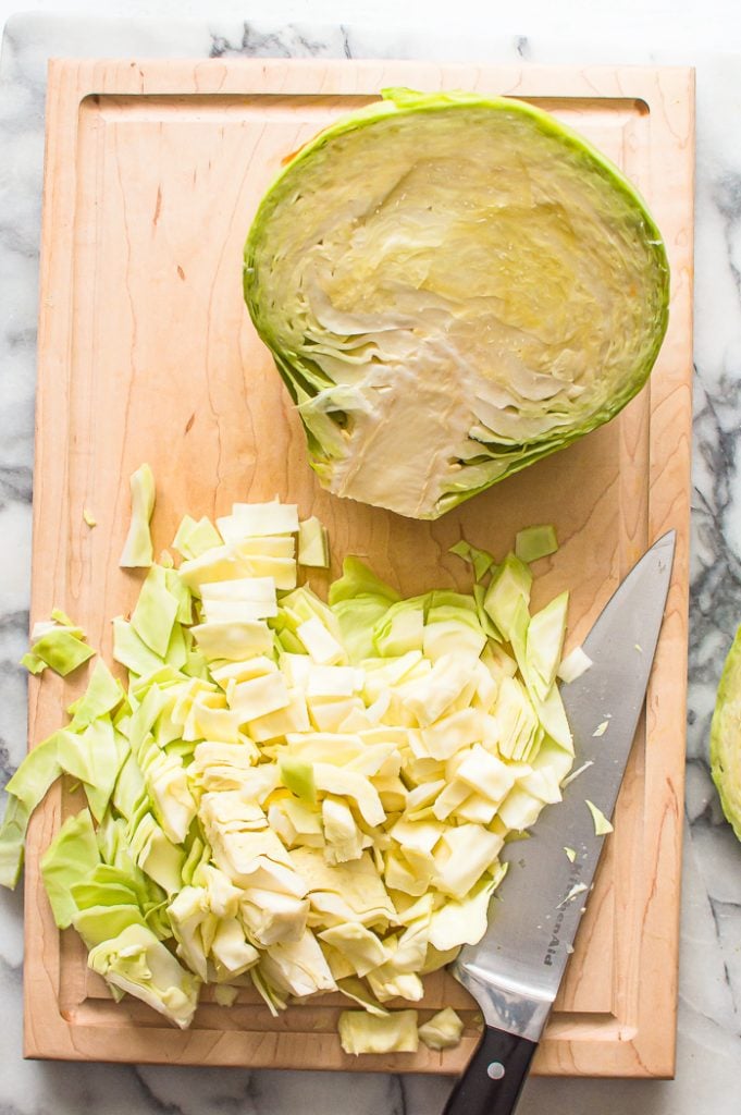 Chopped cabbage on a cutting board with a knife. A cabbage head half is also on the cutting board.